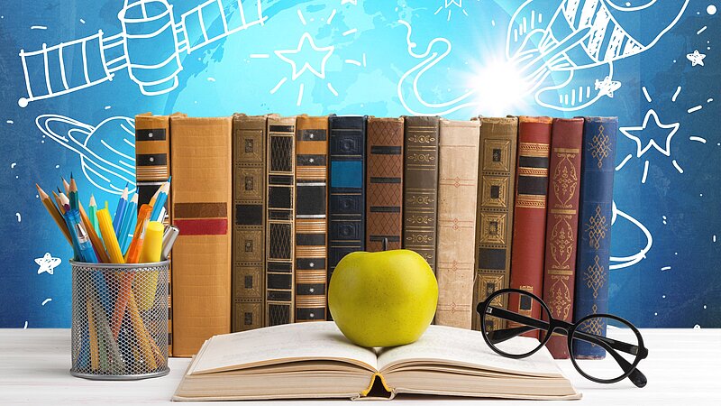 Reihe von Büchern, Bleistiften, Brillen, grüner Apfel auf offenem Buch