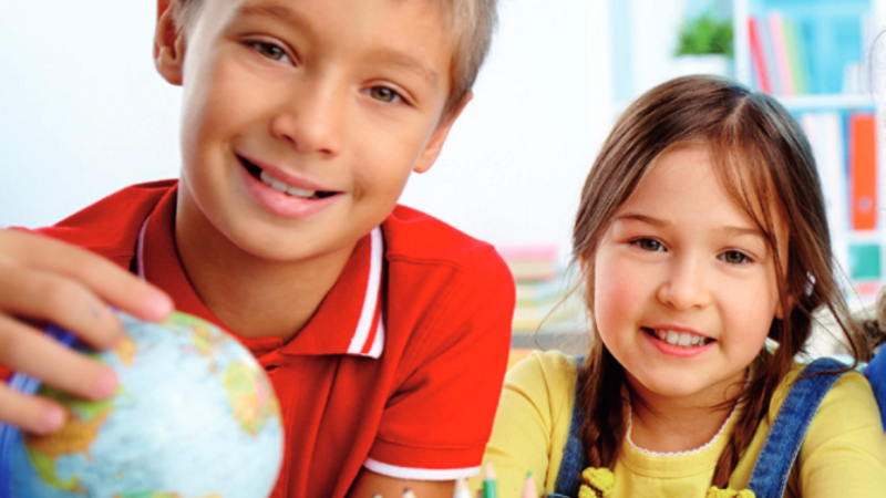 Auf dem Bild ist das Cover des bayerischen LehrplanPLUS für die Grundschule zu sehen. Zwei Kinder sitzen an einem Tisch. Das Kind links hält einen Globus in der Hand, während das Kind rechts auf den Tisch gestützt ist.