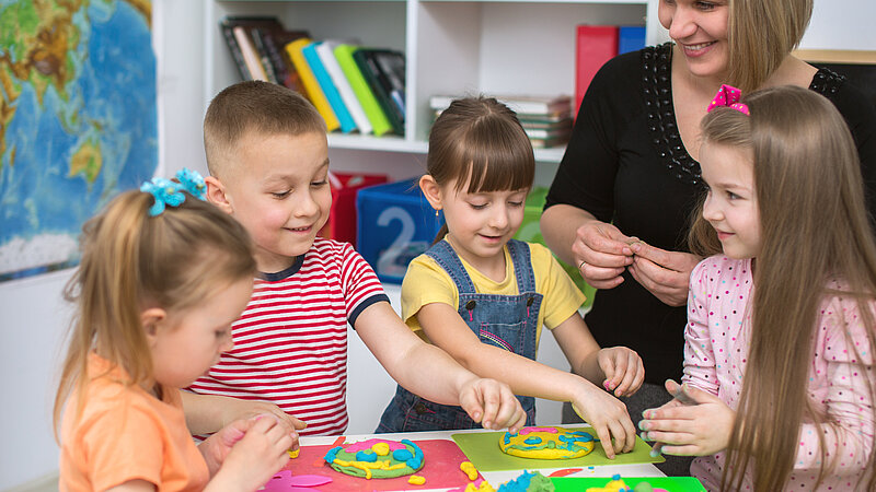 Jüngere Schülerinnen und Schüler mit Lehrerin beim Kneten in Teamarbeit