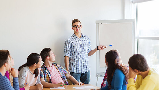 Mann steht vor Flipchart und erklärt Menschen am Besprechungstisch etwas