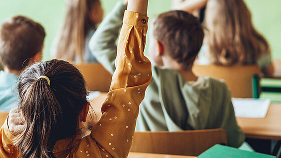 Schulmädchen im Klassenzimmer, das die Hände hebt, um Fragen zu stellen